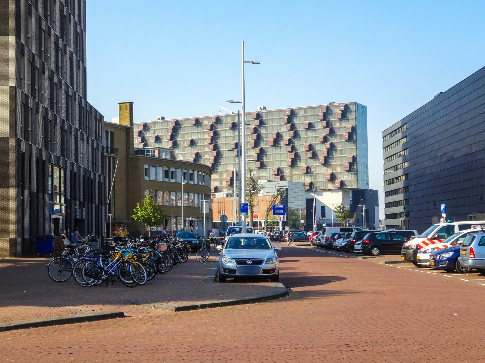 Stadsstraat met een geparkeerde taxi, fietsenrekken en moderne kantoor- en woongebouwen