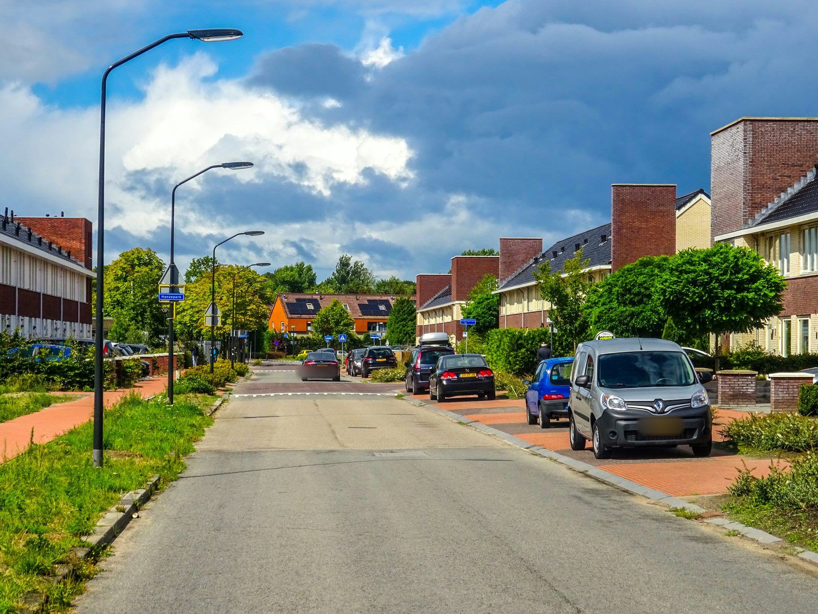 Woonstraat in een nieuwbouwwijk met geparkeerde auto's en een bestelbus onder een wolkenlucht